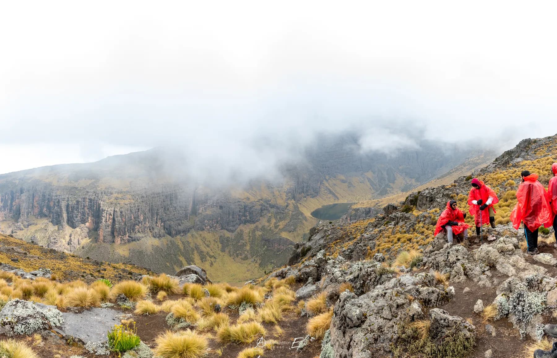Trekkers in red jackets on a rocky ridge above a misty valley on Mount Kenya